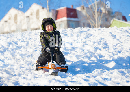 Piccolo 3 anni vecchio ragazzo scorrevole sulla slitta scooter sul giorno di inverno Foto Stock