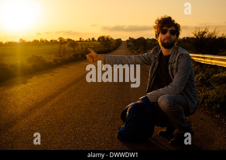 Giovane uomo autostop su una strada di campagna Foto Stock