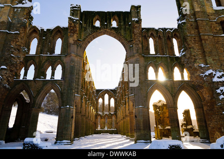 La luce del sole che splende attraverso le finestre ad arco nelle rovine di Rievaulx Abbey sotto una copertura di neve su un luminoso winter's day Foto Stock