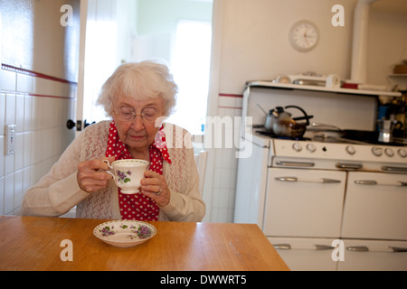 Donna anziana bere il tè in cucina Foto Stock