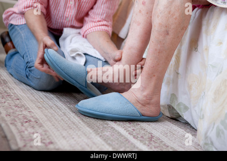 Close-up di donna aiuta donna anziana messo in pantofole Foto Stock