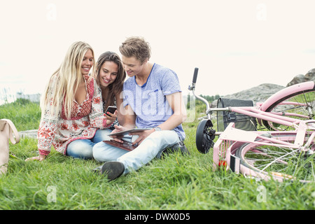 Giovani amici utilizzando il telefono cellulare e la tavoletta digitale in bicicletta sul campo Foto Stock