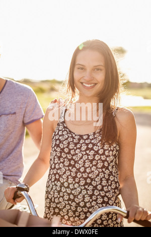 Ritratto di felice giovane donna con la bicicletta in piedi sulla strada di campagna Foto Stock