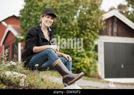 A piena lunghezza Ritratto di fiducioso agricoltore femmina seduto sulla roccia presso l'azienda Foto Stock