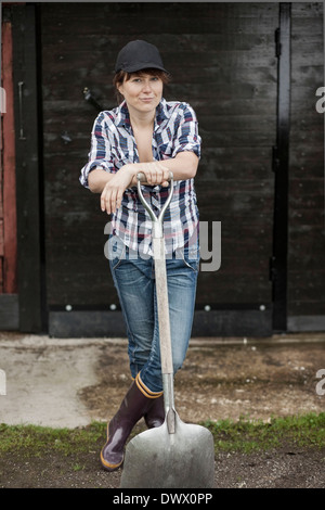 Ritratto di donna fiducioso contadino con la pala in piedi contro il fienile Foto Stock