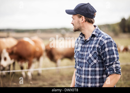 Considerato il contadino in piedi sul campo mentre gli animali pascolano in background Foto Stock