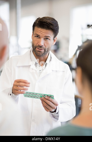 Ingegnere maschio spiegando il circuito stampato per la gente di affari in fabbrica Foto Stock