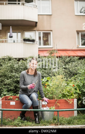 A piena lunghezza ritratto di donna felice con attrezzature da giardinaggio in giardino Foto Stock