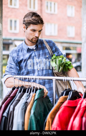 Giovane con negozi di generi alimentari selezionando giacche in negozio di abbigliamento Foto Stock