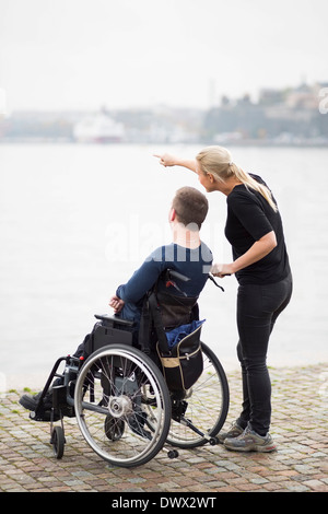 Custode mostrando qualcosa di uomo disabili su sedia a rotelle dal lago Foto Stock