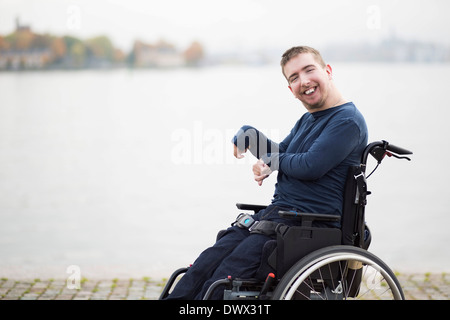 Ritratto di uomo felice con paralisi cerebrale seduto su una sedia a rotelle dal lago Foto Stock