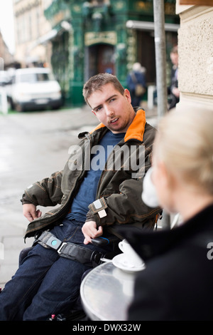 Disabilitato l'uomo con la femmina caretaker sidewalk cafe Foto Stock