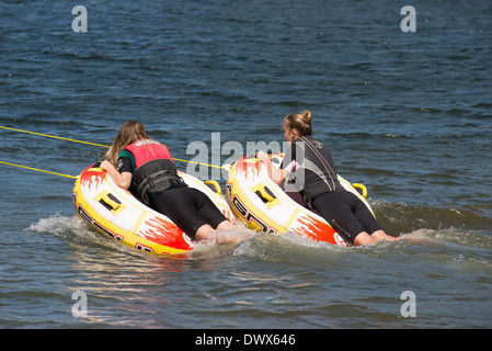 Due ragazze adolescenti ride ciambella gonfiabile trainato da un motoscafo sulle rive di un fiume in Moana Roa Riserva Nord isola NZ Foto Stock