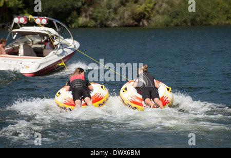 Due ragazze adolescenti ride ciambella gonfiabile trainato da un motoscafo sulle rive di un fiume in Moana Roa Riserva Nord isola NZ Foto Stock