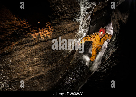 Un speleologo fa la sua strada verso il passaggio del flusso in Ogof Ffynnon Ddu, Brecon Beacons, South Wales, Regno Unito Foto Stock