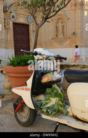 Vecchio motorino scooter con alcuni generi alimentari al di fuori della Chiesa della Visitazione di Gharb. Isola di Gozo. Malta Foto Stock
