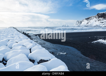 Il basalto nero sabbie e un molo di roccia ricoperti di neve fresca a Vík í Mýrdal sulla costa sud dell'Islanda Foto Stock