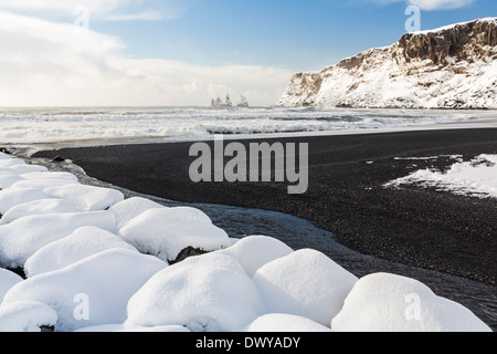 Il basalto nero sabbie e un molo di roccia ricoperti di neve fresca a Vík í Mýrdal sulla costa sud dell'Islanda Foto Stock