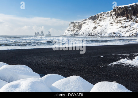 Il basalto nero sabbie e un molo di roccia ricoperti di neve fresca dopo una tempesta in Vík í Mýrdal sulla costa sud dell'Islanda Foto Stock