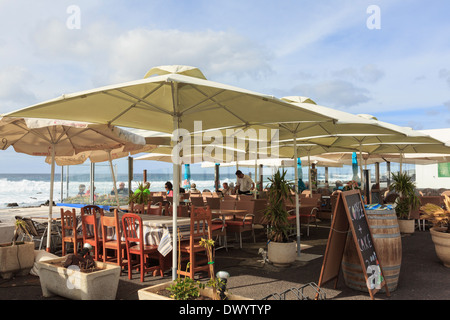 Sala da pranzo di persone sotto gli ombrelloni in un ristorante sul mare in El Golfo, Lanzarote, Isole Canarie, Spagna, Europa. Foto Stock