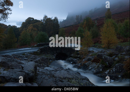 Ponte Ashness inizio in una fredda e nebbiosa mattina d'autunno. Derwent Water lago è visibile in lontananza. Foto Stock