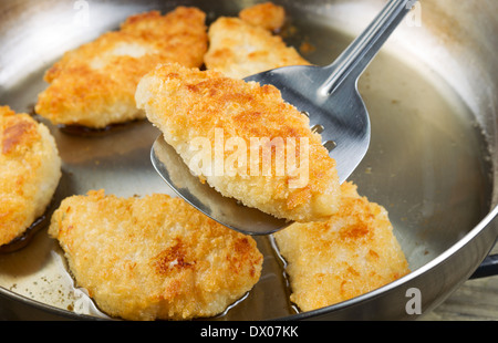 Foto orizzontale di golden impanati rivestito essendo di pesce fritto in acciaio inox padella con focus sul singolo pezzo con la spatola Foto Stock