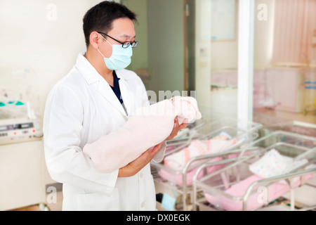 Medico tenendo un neonato in una sala per neonati in ospedale Foto Stock