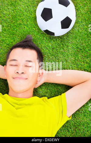 Giovane uomo disteso su un prato con un campo di calcio Foto Stock