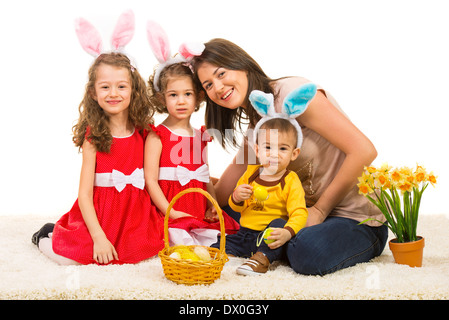 Felice madre con i suoi bambini indossando orecchie di coniglietto seduti insieme sul tappeto di pelliccia Foto Stock