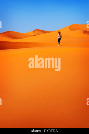 Woman Trekking lungo il caldo deserto, un bel colore arancione dune sabbiose, esplorando Sahara, vacanza attiva alla scoperta di concetto Natura Foto Stock