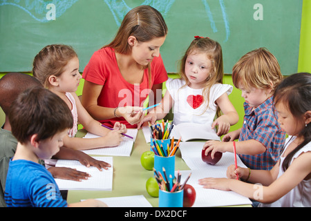 I bambini che imparano la scrittura insieme nell'asilo nido con docente Foto Stock