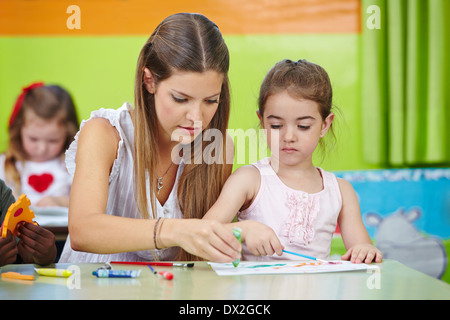 Insegnante di vivaio aiutando la ragazza con la pittura acquerello in un kindergarten Foto Stock