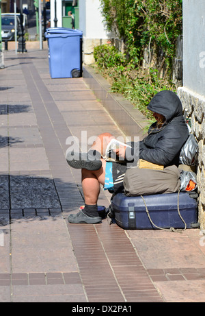 Senzatetto la lettura di un libro di fronte alla chiesa di Fuengirola, Spagna. Foto Stock