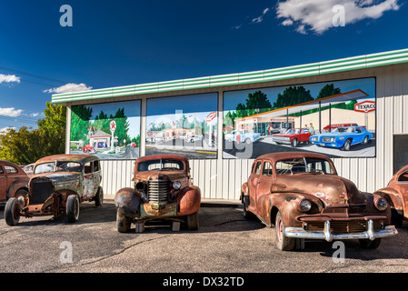 Vecchio, arrugginita automobili per la vendita, murales dietro sulla parete della stazione di servizio, in Delta, Colorado, STATI UNITI D'AMERICA Foto Stock