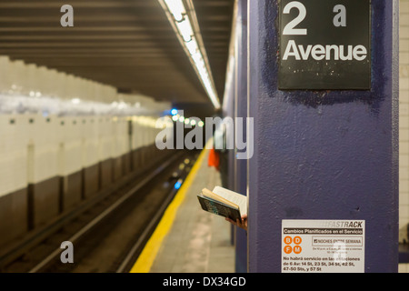 Una donna che legge un libro con la copertina rigida sulla seconda piattaforma Avenue nella metropolitana di New York Foto Stock