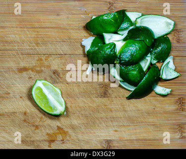 Un singolo pezzo di lime tagliato in attesa di essere sbucciato accanto a bucce da altre limette. Foto Stock