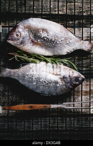 Vista dall'alto sul traino crudo pesce dorado con rosmarino e sale marino sulla griglia sopra il vecchio tavolo in legno. Foto Stock