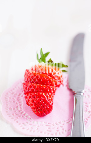 Primo piano di fettine di fragole fresche con argento coltello di metallo in appoggio sul decorativo tappetino rosa Foto Stock