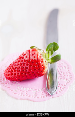 Vista dettagliata del fresco intero di fragola e argento coltello di metallo in appoggio sul decorativo tappetino rosa Foto Stock