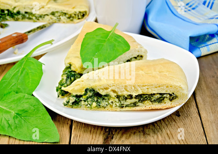 Due pezzi di una torta con spinaci e formaggio su una piastra, foglie di spinaci, coltello, igienico sullo sfondo delle tavole di legno Foto Stock