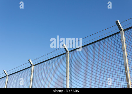 Alti maglia a filo muro di sicurezza su pali di calcestruzzo, guarnita con tre trefoli di filo spinato a 45 grado rivolte verso l'esterno e angolo Foto Stock