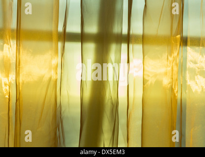 La luce solare attraverso la finestra flussi in una stanza attraverso sottili golden tendine Foto Stock