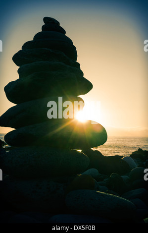 Pietre bilanciato sulla spiaggia e il sole al tramonto. Foto Stock