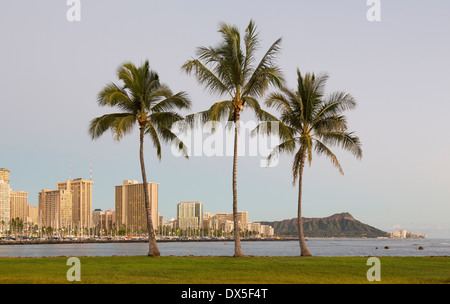 Di Honolulu e Waikiki da Ala Moana Park come il sole tramonta con tre alberi di palma, Hawaii, STATI UNITI D'AMERICA Foto Stock