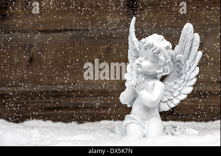 Poco bianco angelo custode in neve su sfondo di legno. in stile vintage decorazione di Natale con la caduta di effetto fiocchi di neve Foto Stock