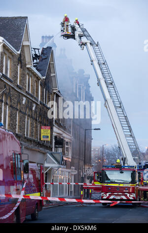 Coraggioso pompiere equipaggio fino ad alta scala (dal motore) affrontare il fuoco con tubo flessibile per acqua, al centro storico edificio - Harrogate, North Yorkshire, Inghilterra, Regno Unito. Foto Stock