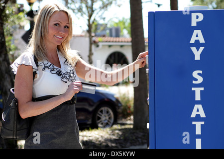 Bella bionda imprenditrice pagando con carta di credito presso il parcheggio della stazione a pagamento Foto Stock