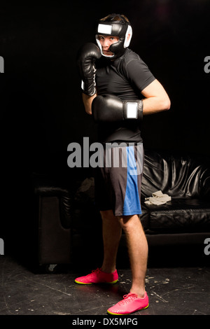 Boxer giovani in attesa di entrare nel ring in piedi nella sua guanti e casco in un atteggiamento vigile in un ambiente buio Foto Stock