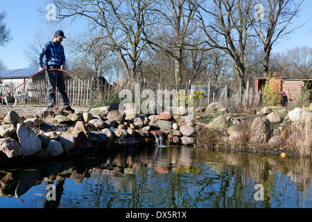 Un uomo si erge a bordo e riempito il laghetto in giardino con acqua fresca Foto Stock