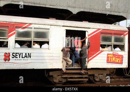 Persone appesi da aprire le porte del treno dei pendolari passando attraverso il Mount Lavinia stazione ferroviaria di Colombo Foto Stock